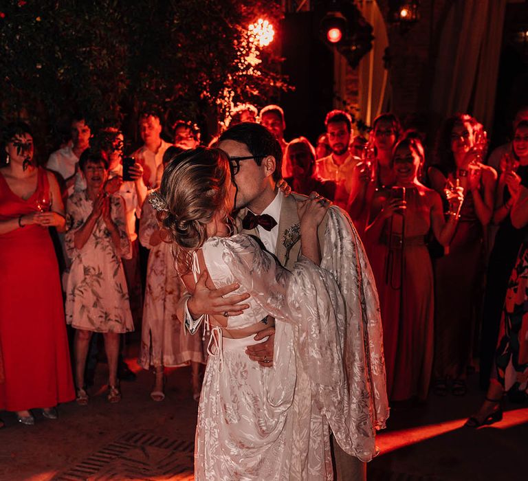 The bride in bridal separates with the groom in cream suit have their first dance together 