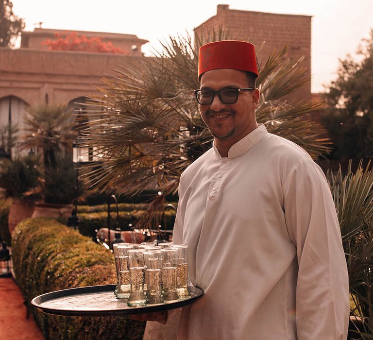 Wedding server in fez hat holding tray of wedding drinks 