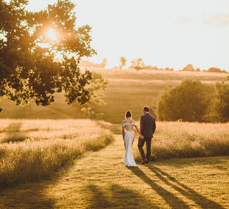 Groom in grey checkered suit with walking around the fields of Hampshire at the wedding venue with the bride in an off the shoulder gown