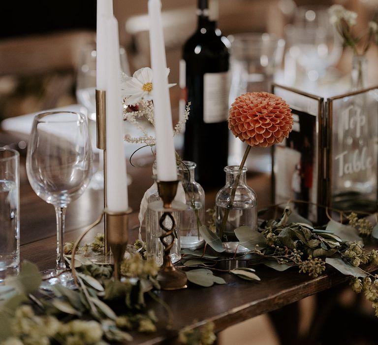 White taper candles, bud vases filled with dahlias in neutral peach tone with photo frame wedding table name sign 