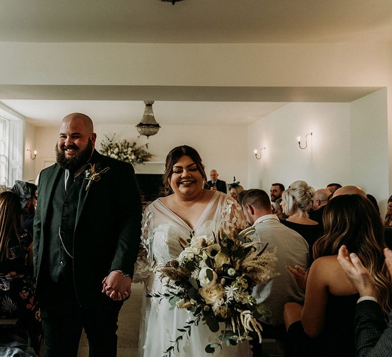 Groom in green tweed wedding suit walking back down the aisle with the bride as a married couple 