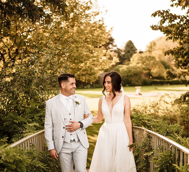 Bride in a shimmering wedding dress and groom in a blue three-piece suit at Oxfordshire wedding venue landscaped gardens 