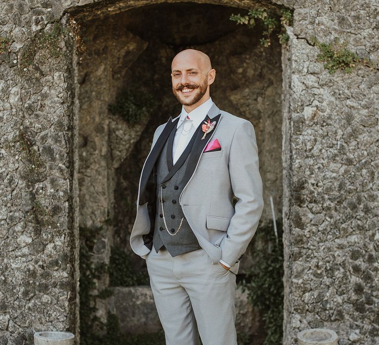 stylish groom in a three piece grey wedding suit with pink pocket square 