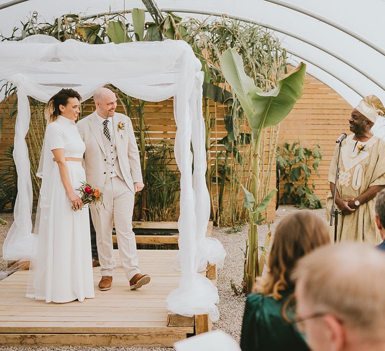 White wedding drapes decorating canopy at polytunnel greenhouse ceremony with father of the bride performing a reading 