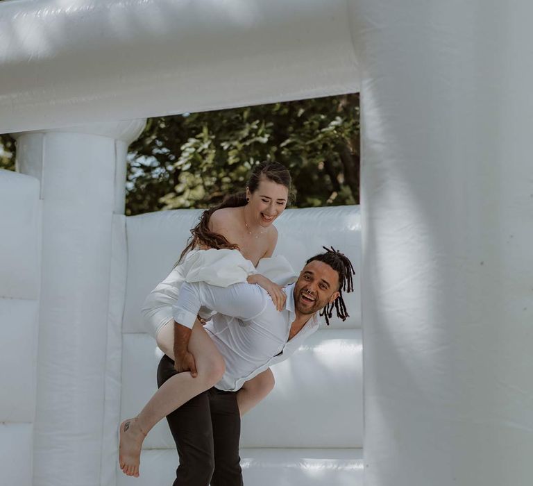 Bride and groom playing on outdoor wedding bouncy castle 