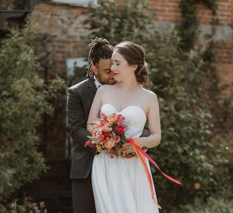 Bride in strapless sweetheart neckline wedding dress holding pink and orange wedding bouquet with groom in classic black tuxedo with bowtie and pink and orange wedding boutonniere at The Old Rectory Berkshire