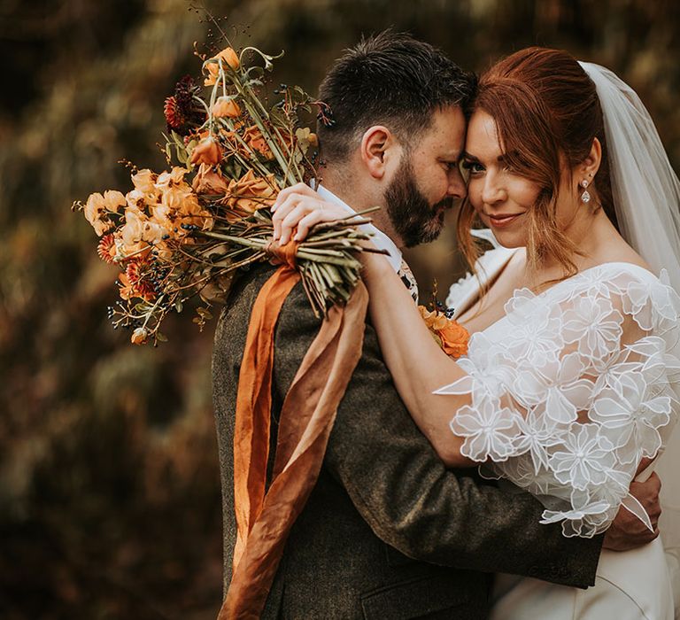 Autumn bouquet tied with ribbon with the bride in a boho flower sleeve wedding dress with groom in three piece suit 