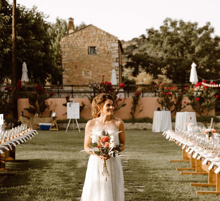 boho bride in a lace wedding dress holding an orange rose bouquet at outdoor destination wedding reception