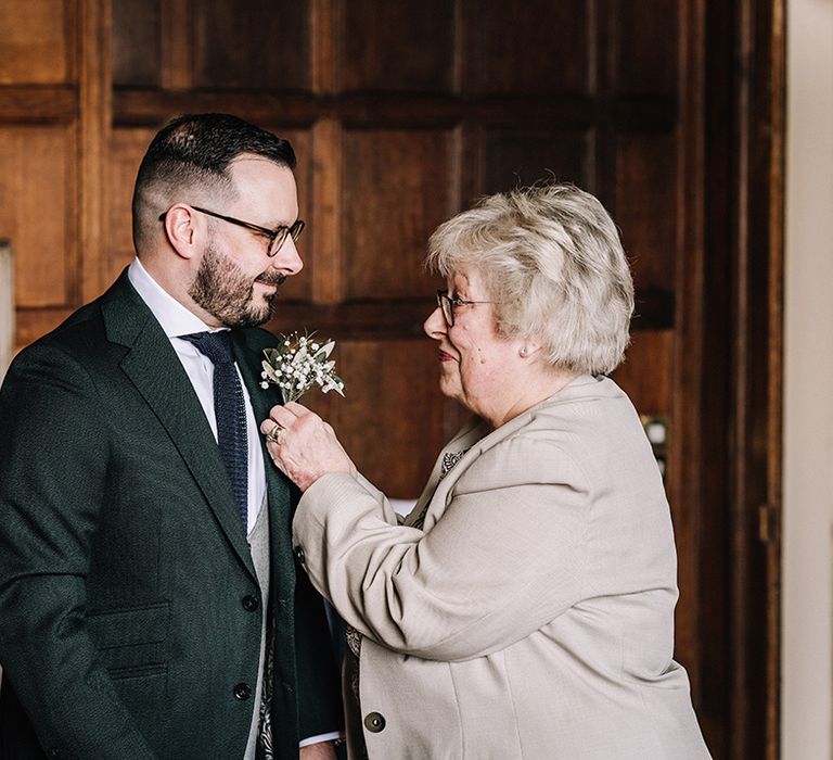 Mother of the groom fixing the buttonhole onto the groom's suit 