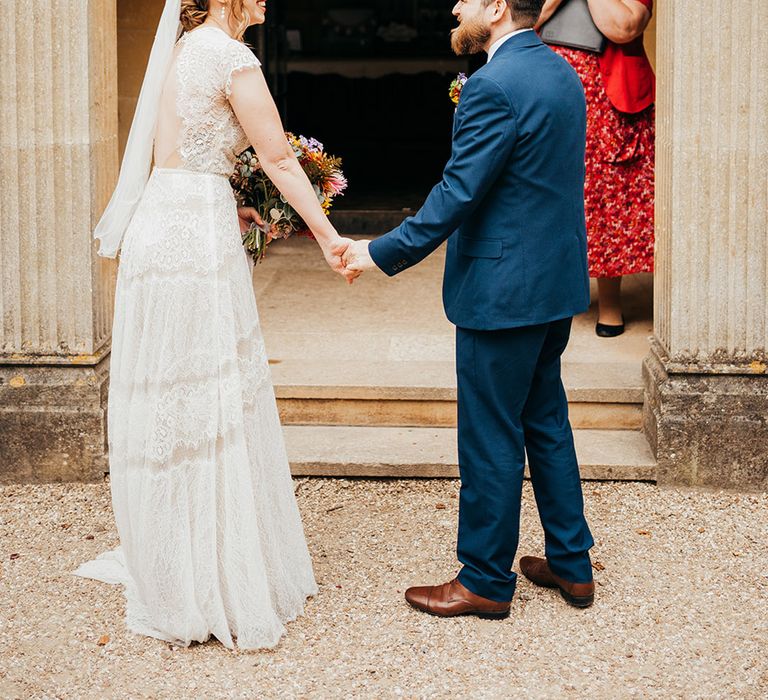 Groom in navy three piece suit with the bride wearing a veil and delicate Willowy by Watters gown for outdoor wedding 