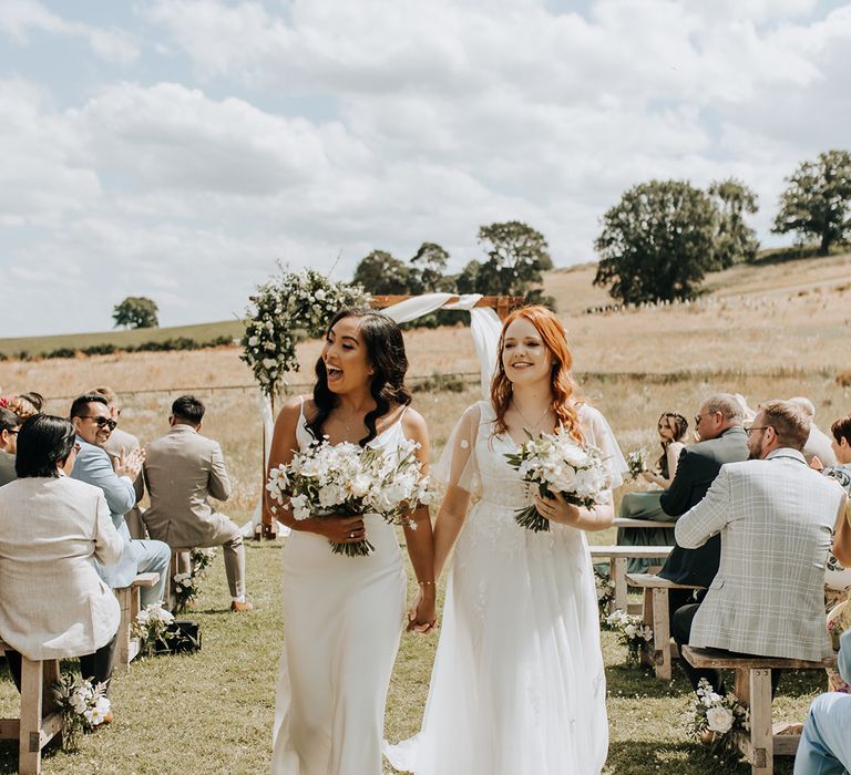 The two brides walk back down the aisle together as a married couple 