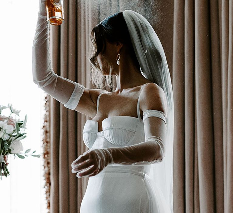 Bride in wedding dress and veil spraying wedding perfume 