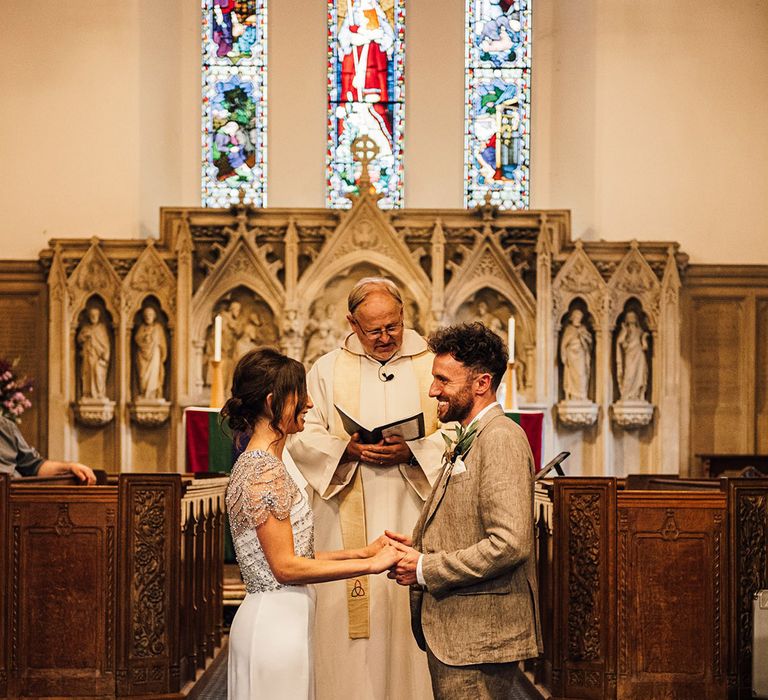 Church wedding ceremony with bride in a beaded sparkly wedding dress and the groom in a grey suit and linen shirt 