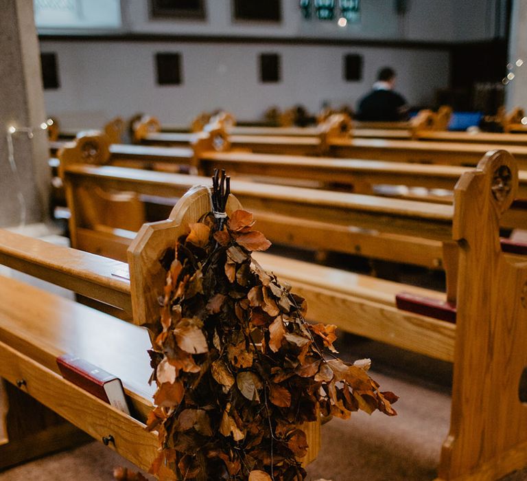 Rustic autumn leaves decorate the pew at the church wedding ceremony 