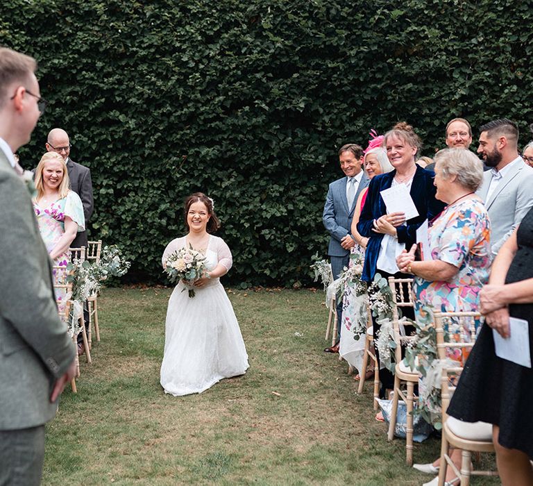 Bride in three quarter length sleeve lace wedding dress walking down the aisle by herself to meet the groom 