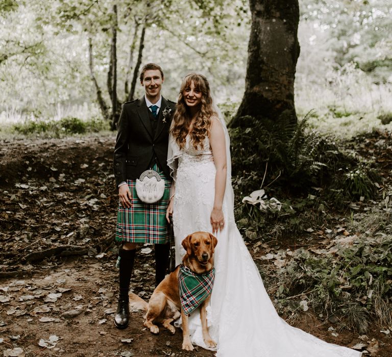 Bride in sparkly floral wedding dress next to groom in traditional Scottish dress with a kilt featuring their dog in the matching family pattern