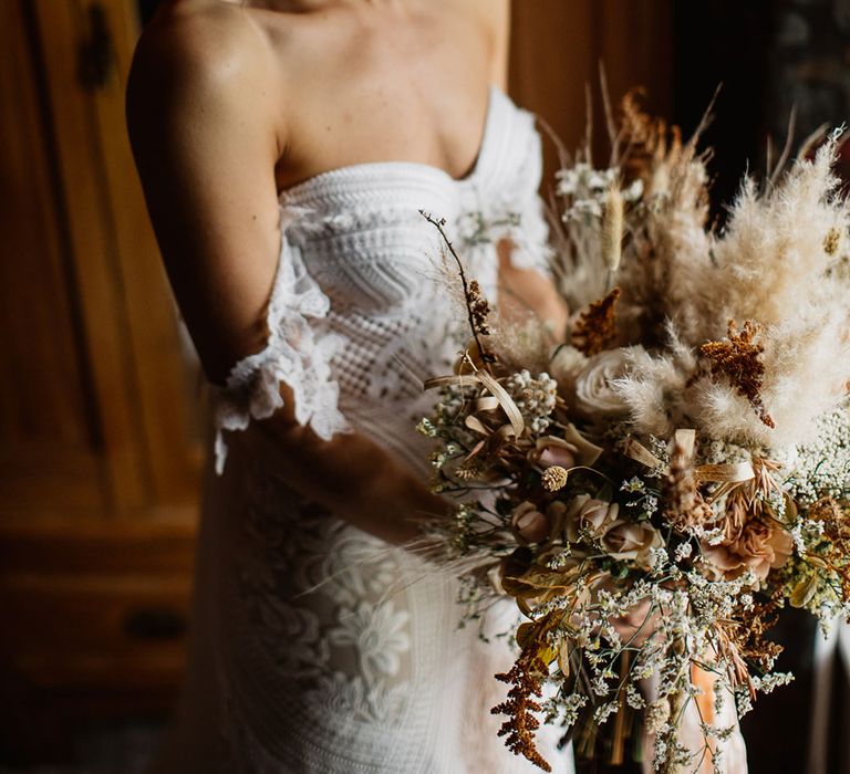 Bride holding white rose and pampas grass bouquet standing by window