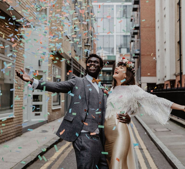 Couple hold arms out as confetti falls on them in city wedding 