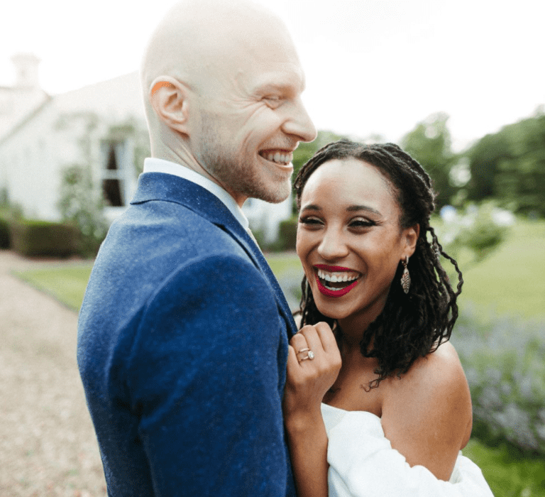 Bride and groom hug and the bride smiles to the camera with fine twisted braids in her hair