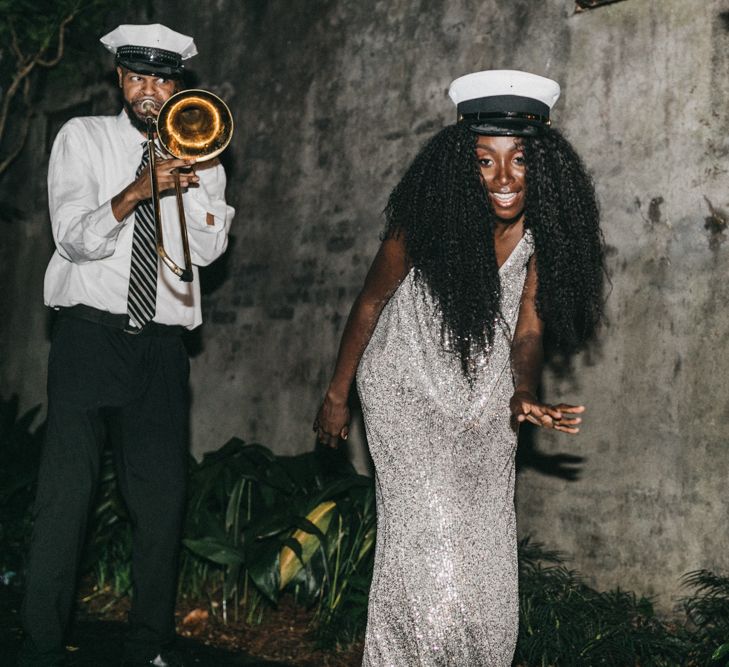 A Black bride with long curly hair laughs to camera as she wears a hat and gold sequinned dress