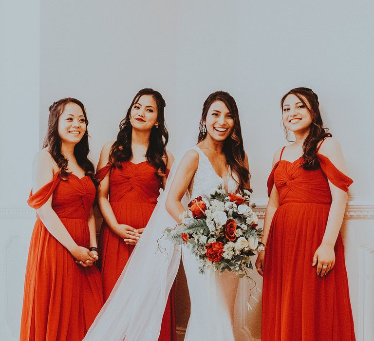 Bride stands with bridesmaids wearing red dresses 