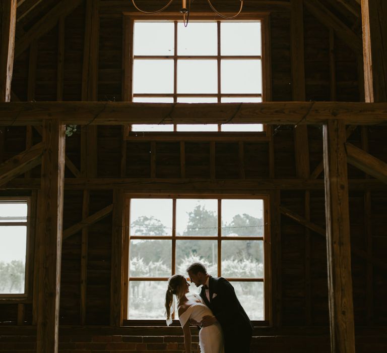 Groom leans back the bride in front of large barn window