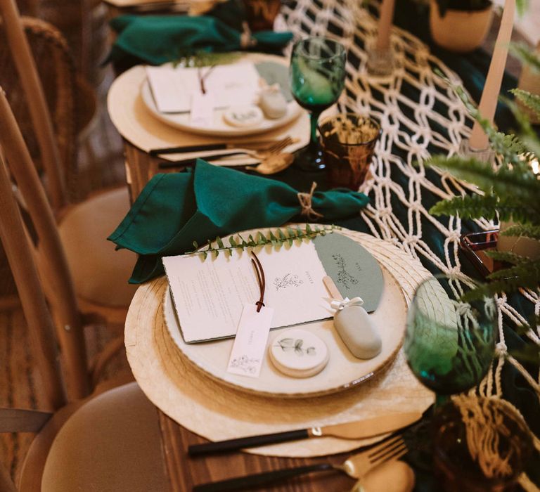 Tablescape featuring green napkins, macrame table runner and wedding stationery