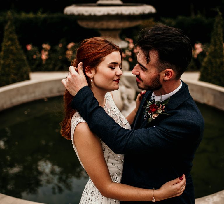 Bride & groom stand in front of fountain as groom caresses brides hair