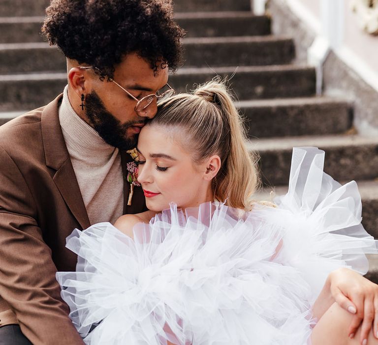 Bride in a short ruffle wedding dress siting with her groom on the steps 