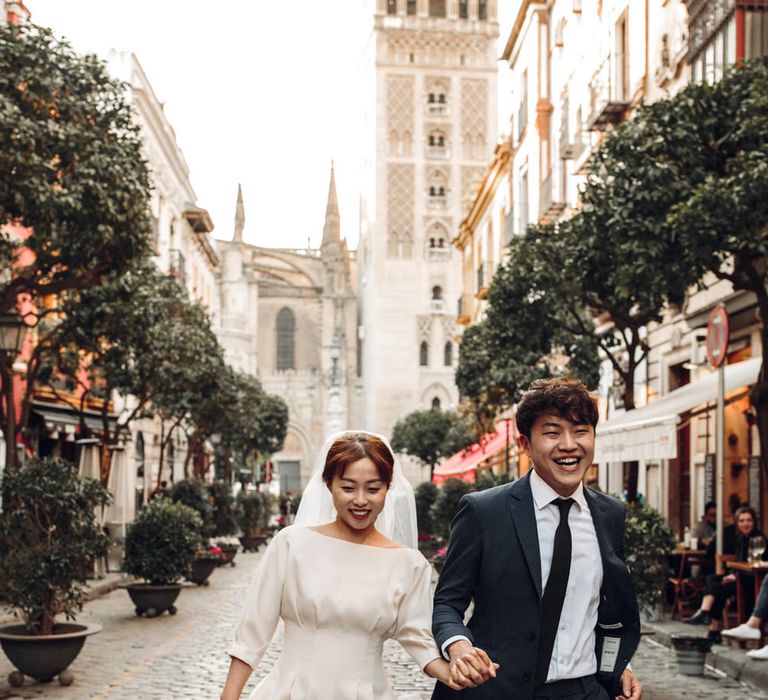 Couple run laughing down market street in Seville