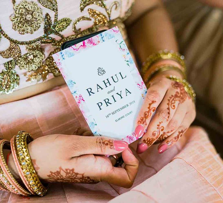 Bride with henna and gold jewellery holding pink floral wedding invitations