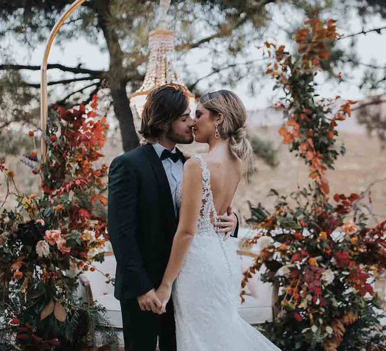 Bride and groom kiss in front of Autumn colour wedding flowers