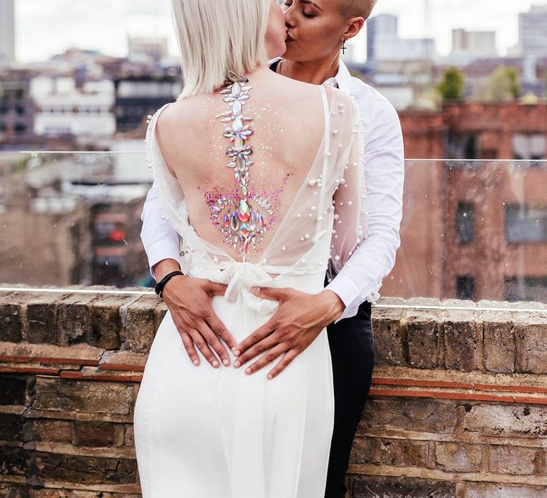 Bride with short hair kissing her bride with jewel body art on her back 