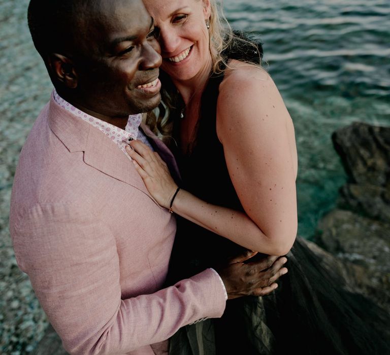 Bride hugs groom who is wearing pink linen style wedding jacket