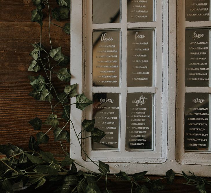 A close up of a table plan written on a white framed glass window. The names are written in white pen.