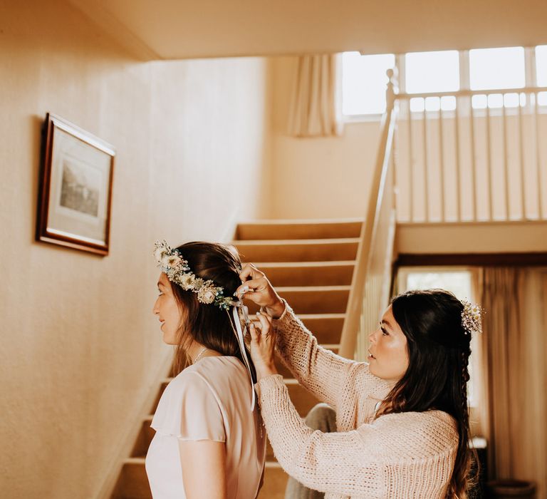 Bride with flowers in her hair adjust bridesmaids flower crown in hallway before wedding