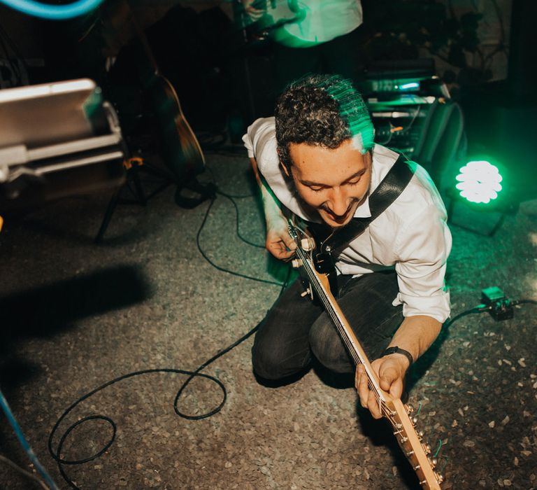 Man in white shirt and black jeans crouches gown with electric guitar on stage at Anran Devon for wedding