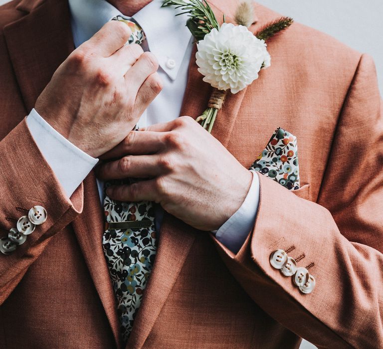 Groom does up his tie on wedding day as he wears floral buttonhole and colourful tie 