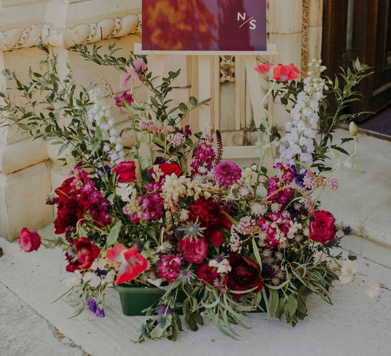 Burgundy acrylic wedding welcome sign with gold font and low vibrant floral arrangement 