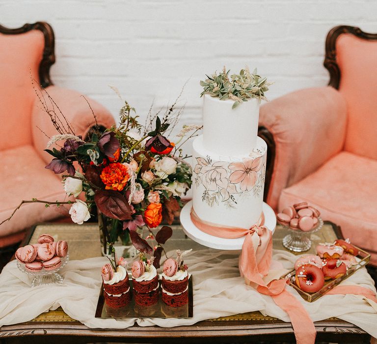 Dessert table with hand painted wedding cake, doughnuts, macaroons and individual cakes 