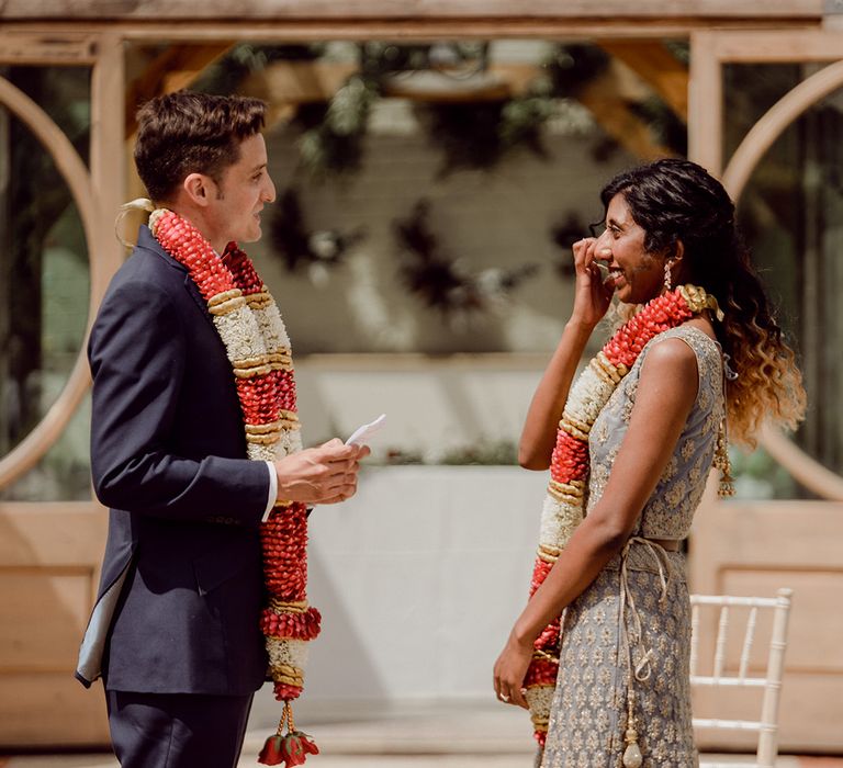 Bride & groom say their vows during Humanist wedding ceremony outdoors whilst wearing colourful garlands around their necks | Joshua Gooding Photography