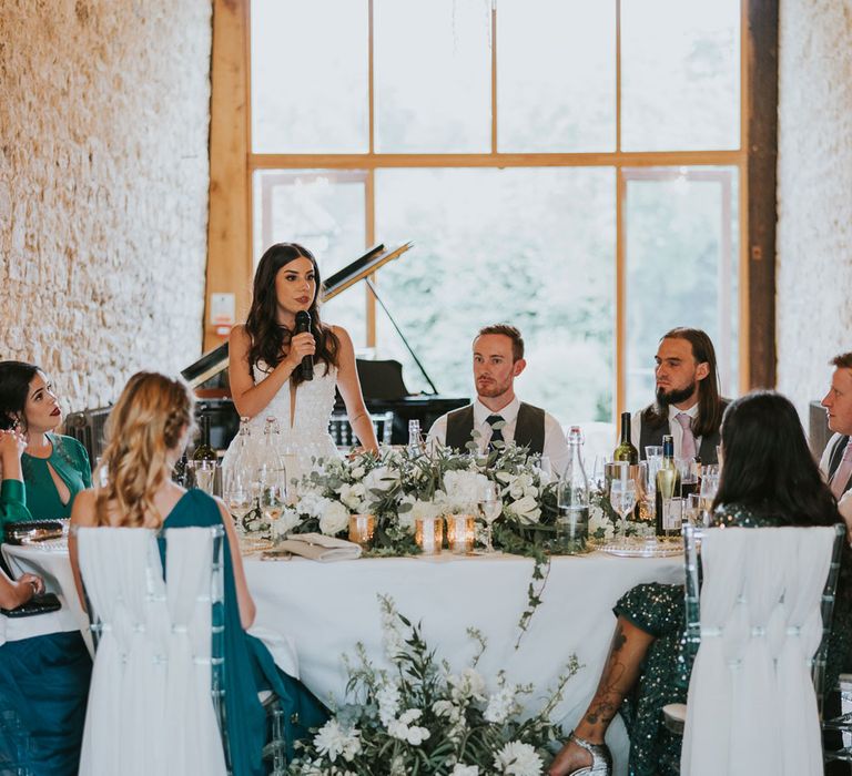 Bride in Pronovias wedding dress makes bride speech during wedding reception at Notley Abbey from round top table with groom, groomsmen and bridesmaids