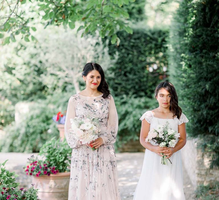 Bridesmaid walks with flower girl whilst holding floral bouquets 