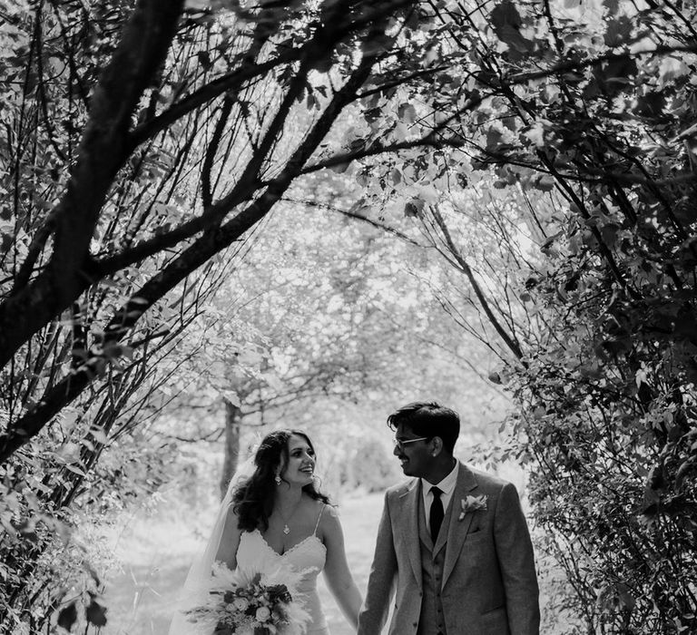 Bride & groom walk hand in hand with one another through the countryside on their wedding day