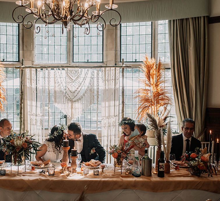 Bride & groom kiss in front of bay window for boho chic styled wedding day