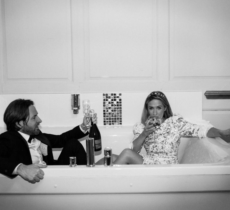 Bride & groom sit in bathtub on their wedding day in black & white image 