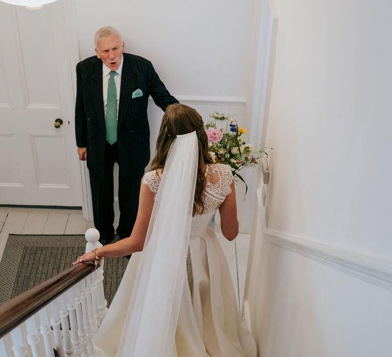 Bride walks down stairs to greet her family member in sage green tie and black pinstriped suit