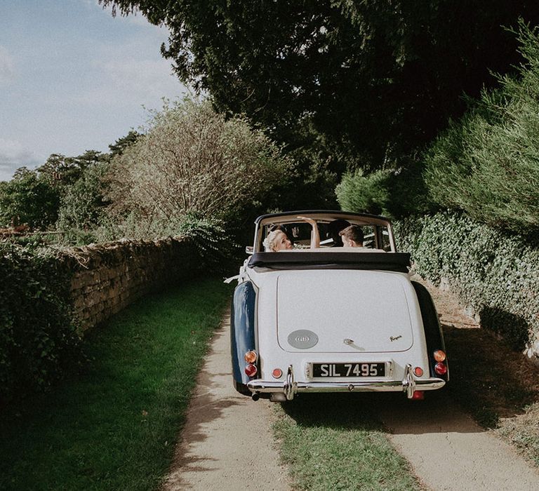 Vintage black and white roof down car escorts the bride and groom away