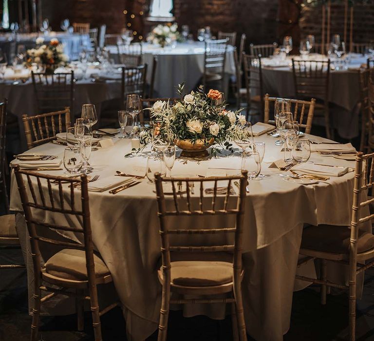 Tablescape with gold cutlery and gold-rimmed glasses with orange and white flower arrangement in golden vase 