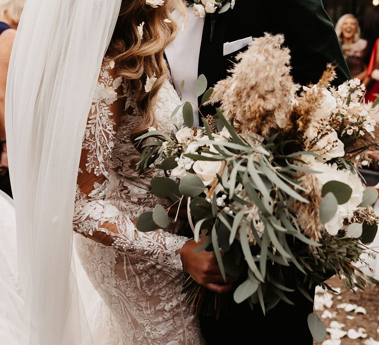 Groom in green velvet suit jacket shares a kiss with the bride who holds white rose and dried flower wedding bouquet